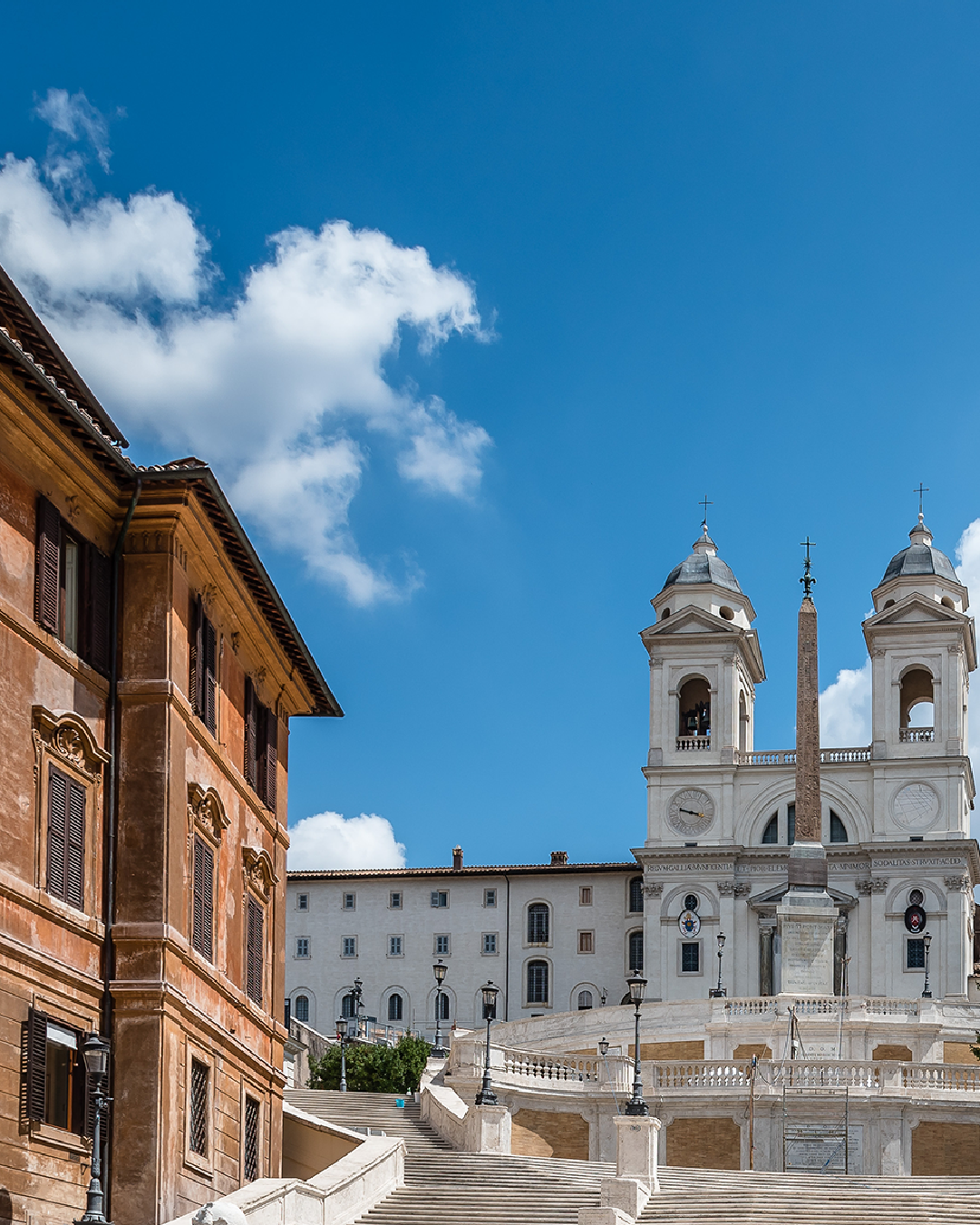 Scalinata di Piazza di Spagna con la chiesa di Trinità dei Monti e obelisco sotto cielo azzurro.