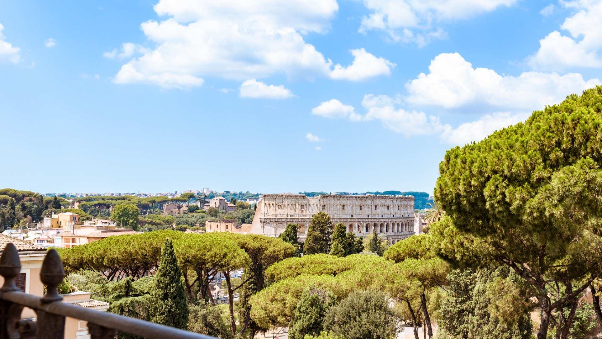 Panorama sul Colosseo immerso nel verde del parco, sotto cielo azzurro con nuvole.
