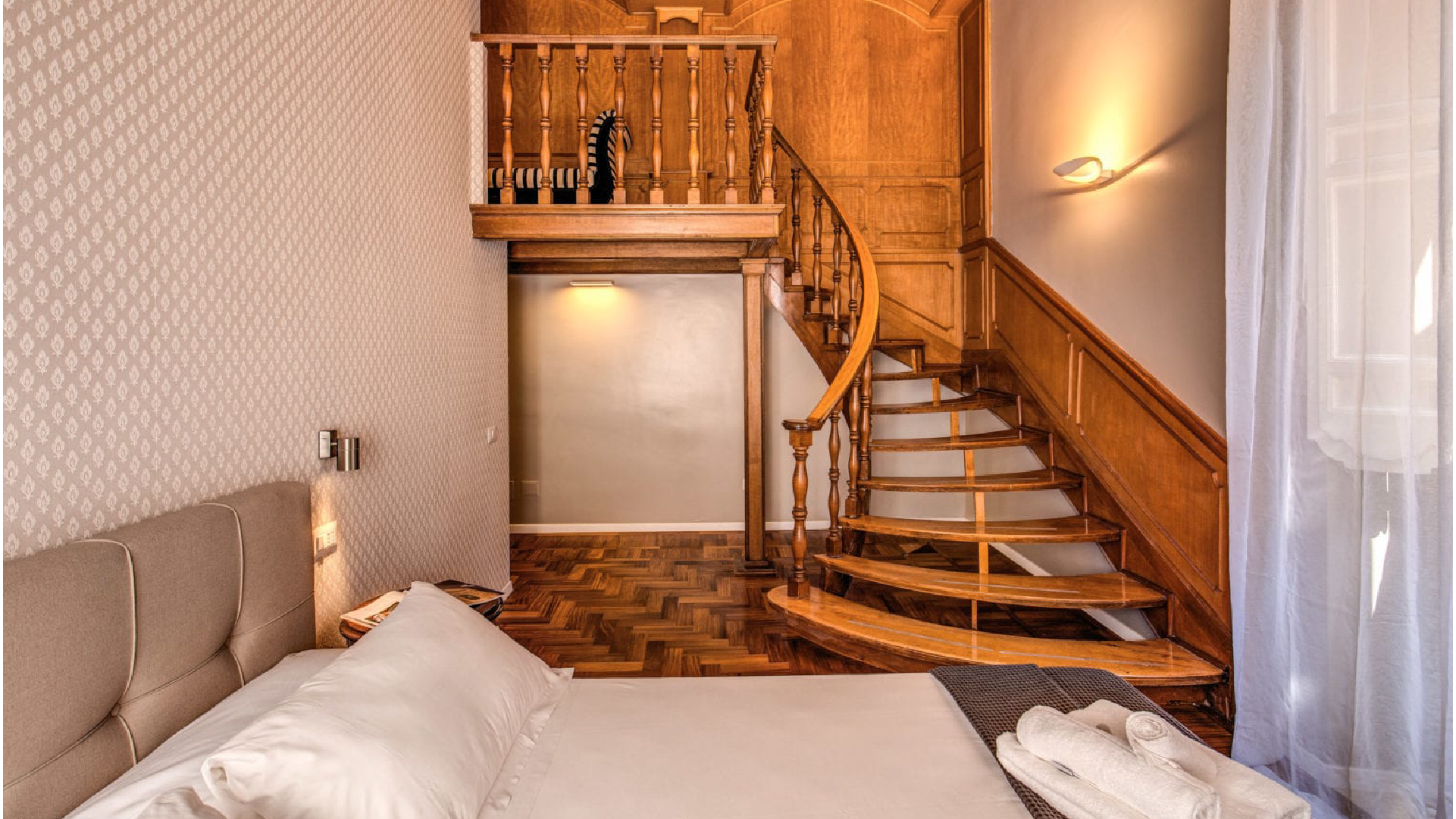 Camera Suite Executive con letto matrimoniale, parquet e grandi finestre con tende leggere, atmosfera elegante e accogliente.